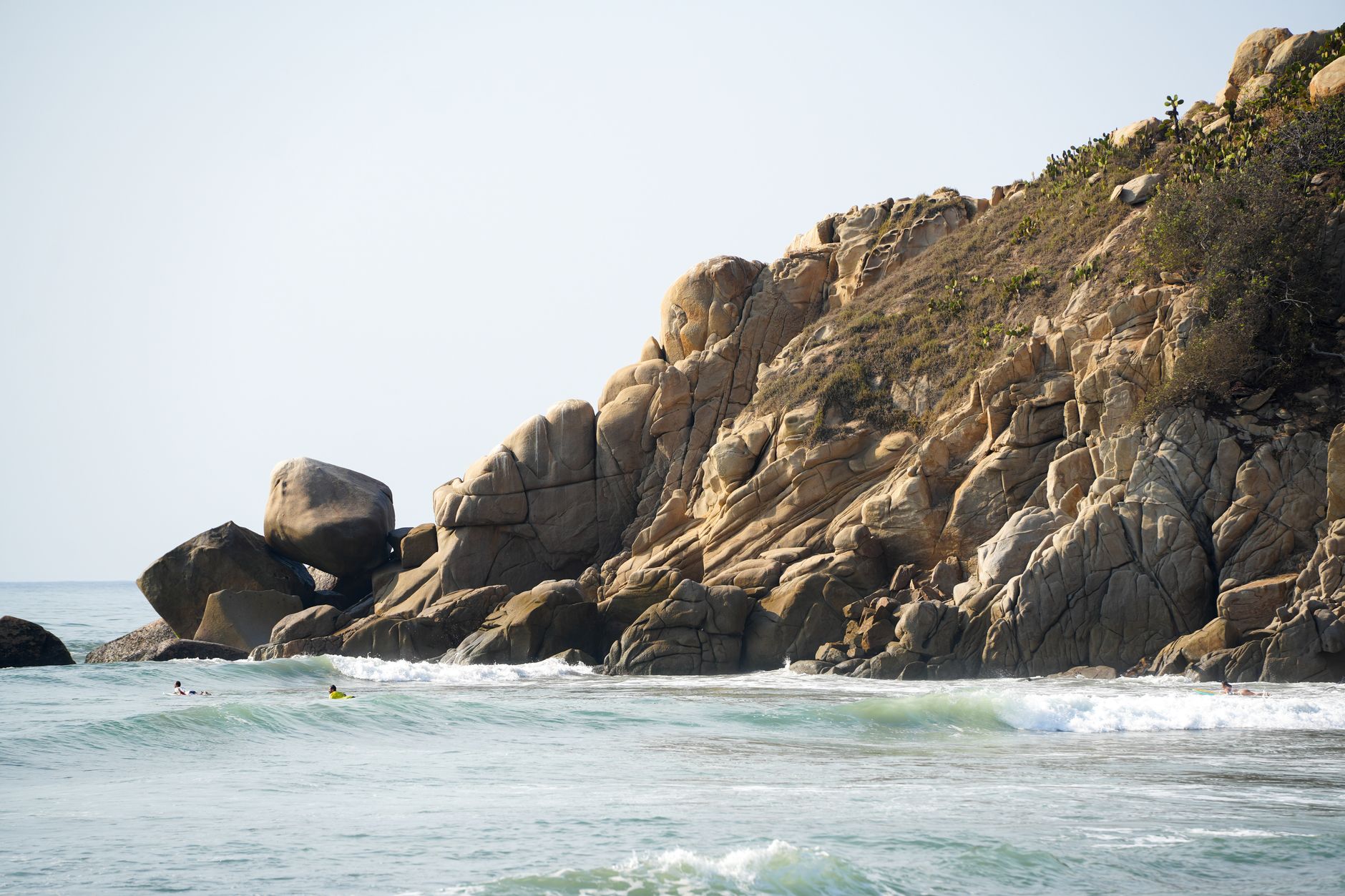 Dramatic ocean waves hit the rocky cliffs of Barra de la Cruz, Oaxaca, under the bright sun.