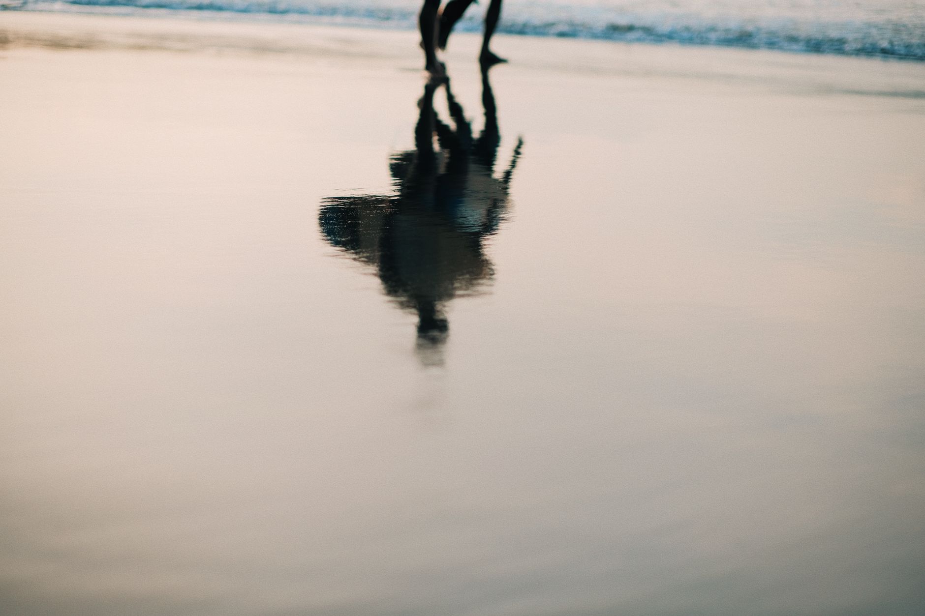 Blurred reflection of surfers walking on a wet beach surface at dusk, capturing a serene and tranquil moment.