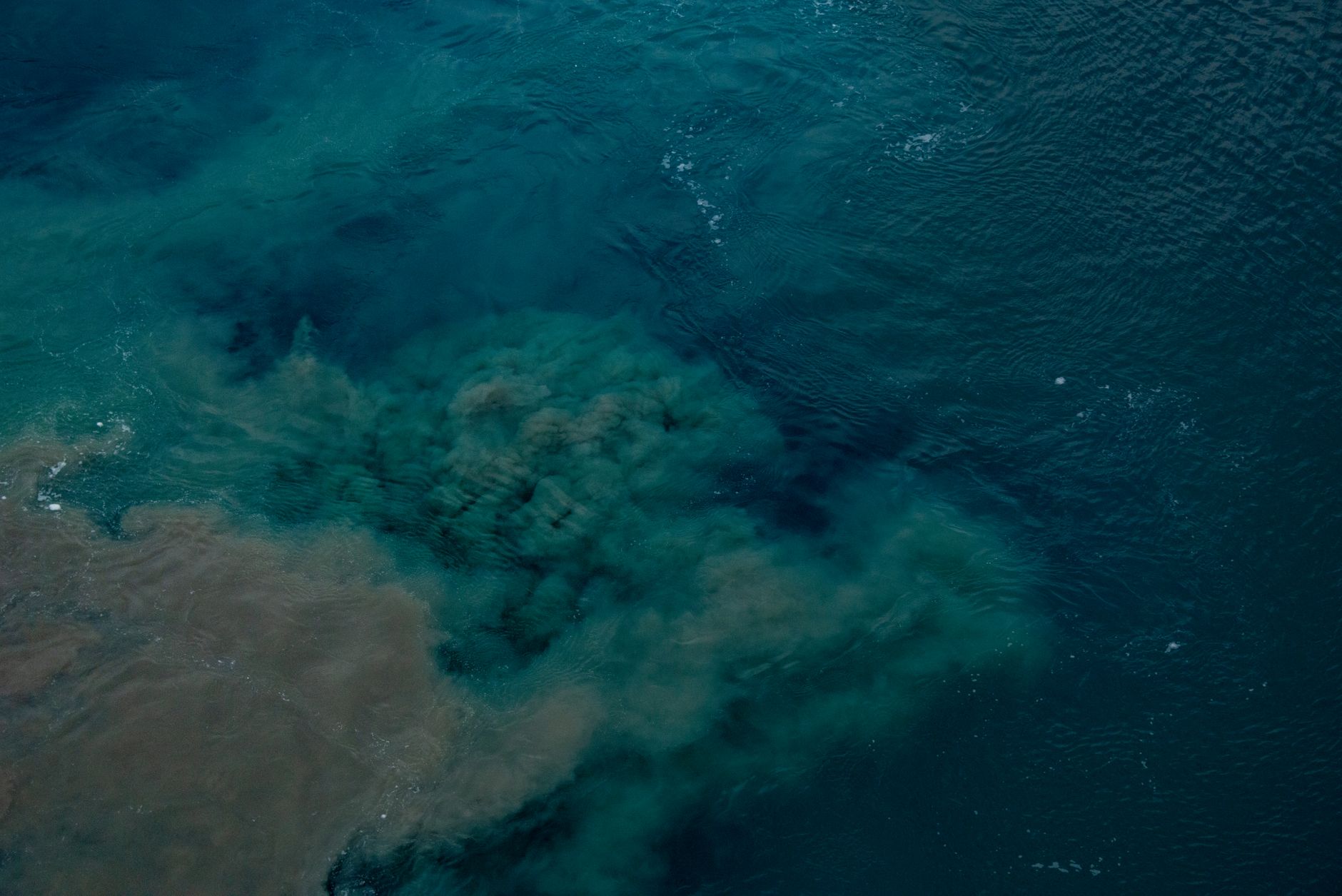 Aerial shot of ocean waters highlighting visible pollution patterns beneath the surface.