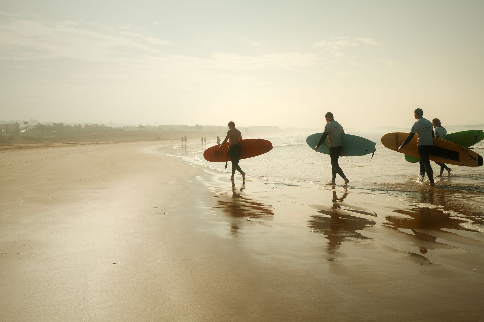 A group of surfers walking towards the ocean on a Moroccan beach at sunset.