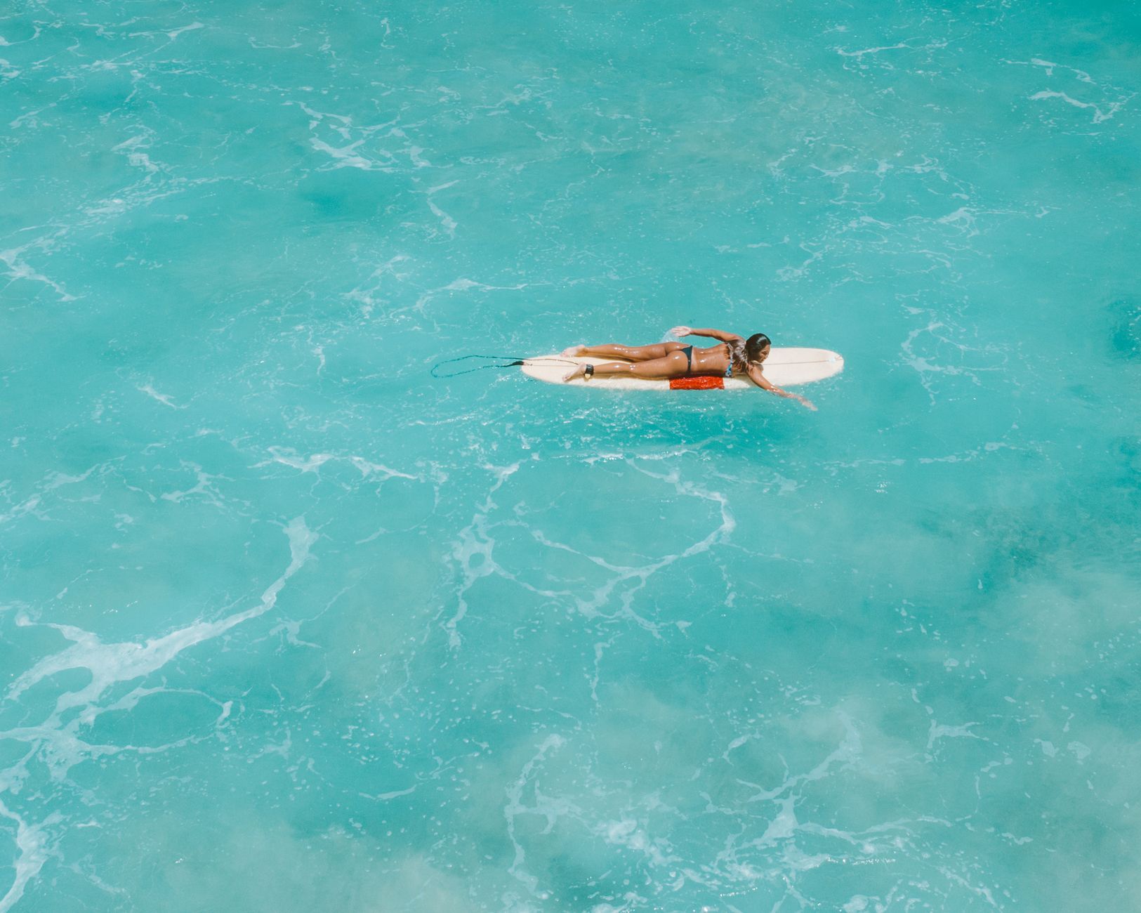 Aerial view of a surfer paddling through clear turquoise waters in Hawaii's coastal paradise.