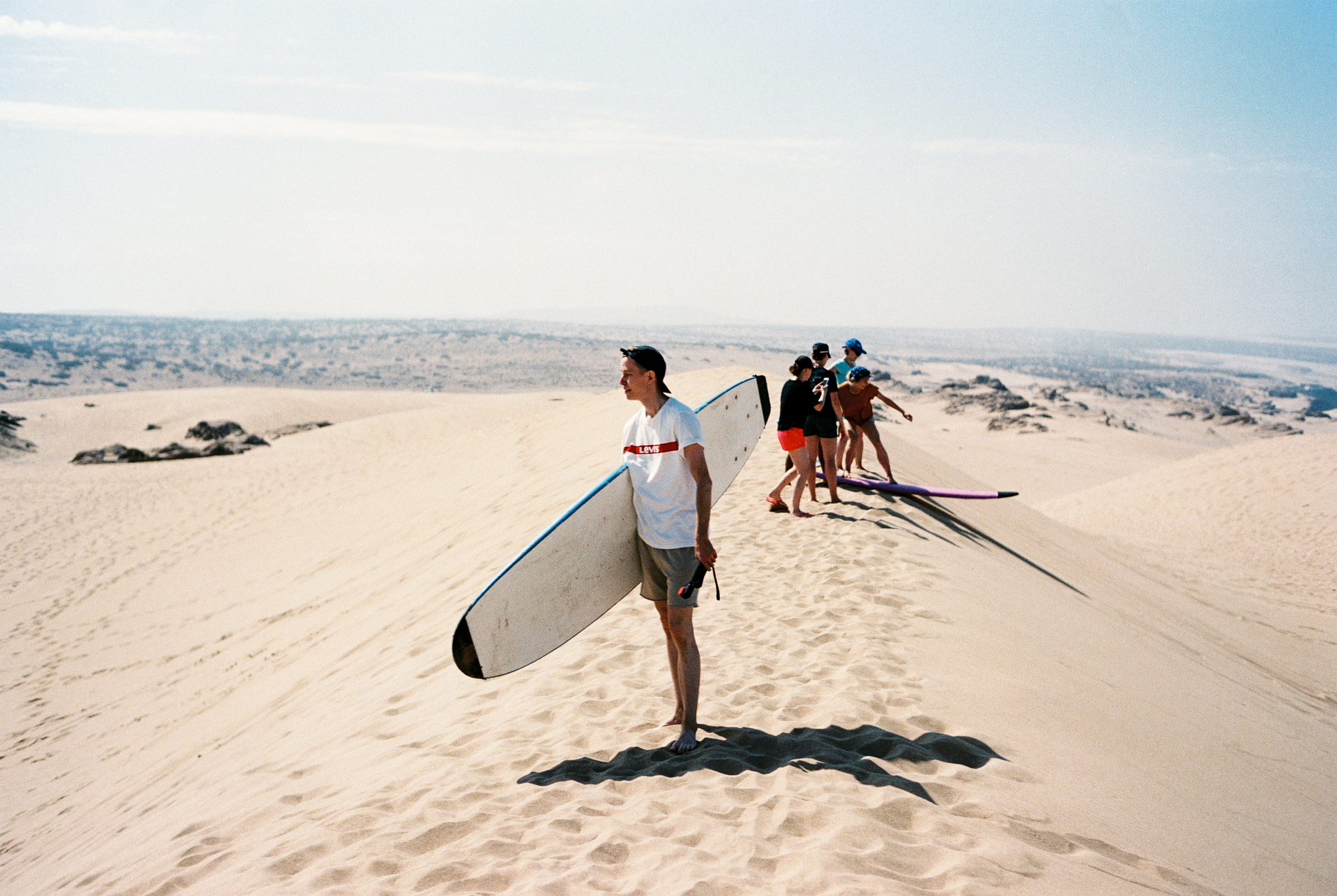 A group of surfers carrying surfboards across sandy dunes in Morocco, perfect for summer adventures.